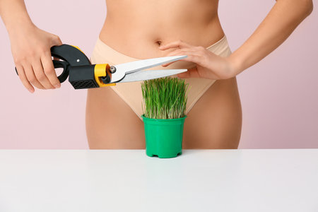 Beautiful young woman with green grass and scissors on pink background, closeup. Depilation conceptの写真素材