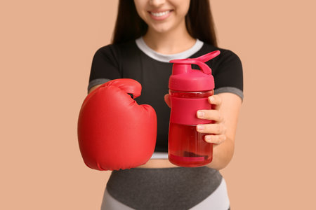 Beautiful young happy woman in boxing gloves with sports bottle of water on beige background, closeupの写真素材