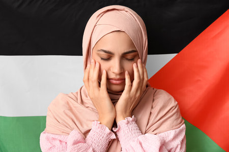 Beautiful young sad Muslim woman against Palestine flag as background. Sorrow conceptの写真素材