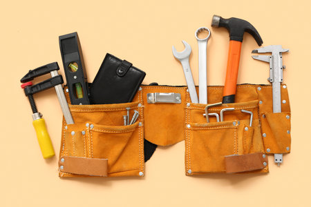 Belt with different construction tools and wallet on beige background