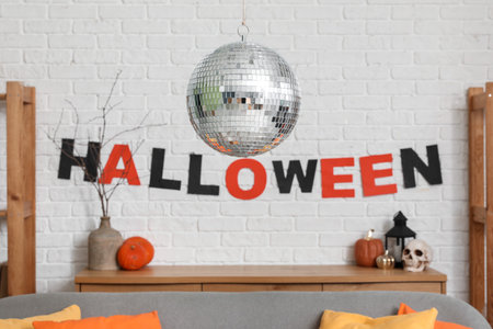 Disco ball and garland with the word HALLOWEEN on white brick wall in room decorated for partyの写真素材