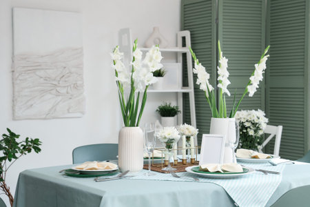 Table setting with white Gladiolus flowers and burning candles in room