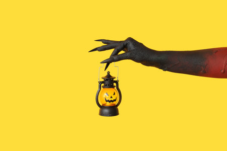 Black hand of witch with jack-o-lantern on yellow background. Halloween celebrationの写真素材