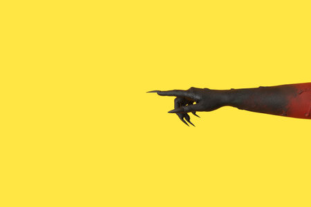Black hand of witch pointing at something on yellow background. Halloween celebrationの写真素材