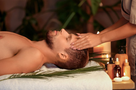 Young man getting treatment head massage on couch in dark spa salonの写真素材