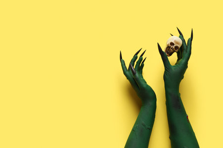 Green hands of witch with claws and human skull on yellow background. Halloween celebrationの写真素材