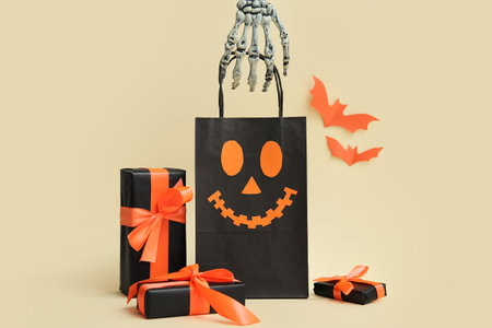 Skeleton hand with shopping bag and Halloween gift boxes on beige backgroundの写真素材