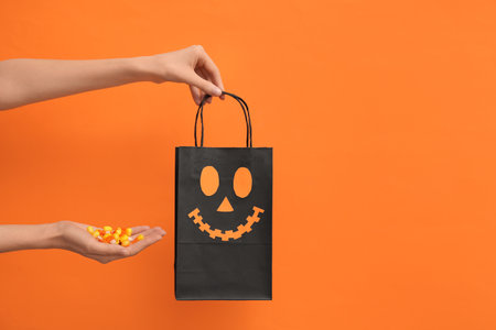 Female hands with Halloween shopping bag and treats on orange backgroundの写真素材