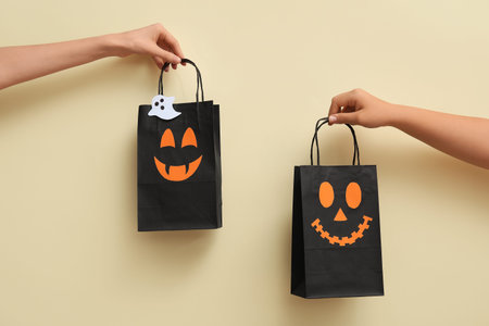 Female hands with Halloween shopping bags on beige backgroundの写真素材