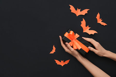 Female hands with Halloween gift and paper bats on black background. Top viewの写真素材