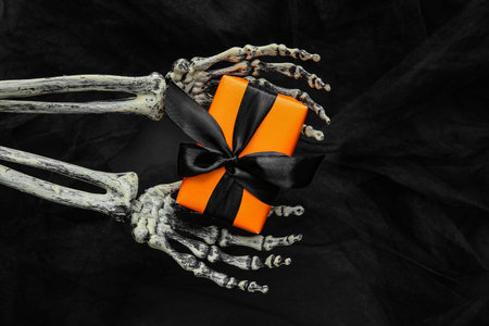 Halloween gifts, skeleton hands and tulle on black background. Top view