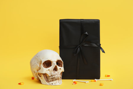 Halloween gift box with decorative skull and treats on yellow backgroundの写真素材