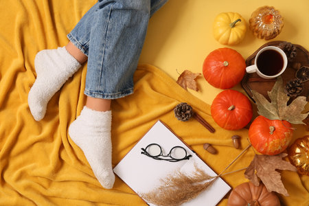 Female legs in warm socks with autumn leaves, pumpkins, plaid and cup of tea on yellow backgroundの写真素材
