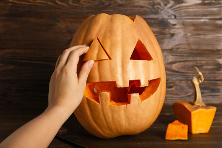 Female hand with carved Halloween pumpkin on wooden backgroundの写真素材