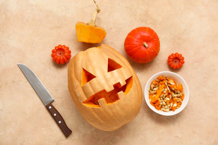 Carved Halloween pumpkin with knife, candles and seeds on beige grunge backgroundの写真素材