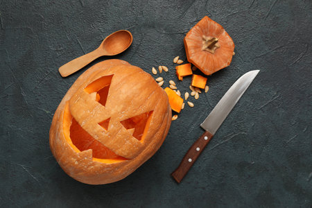 Carved Halloween pumpkin with knife, seeds and wooden spoon on dark blue backgroundの写真素材