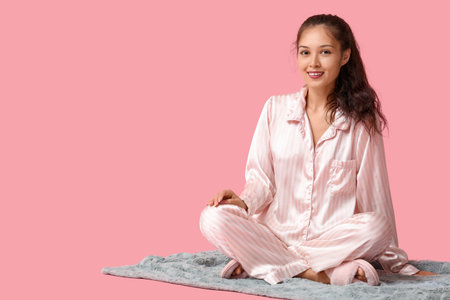 Beautiful young happy Asian woman in pajamas with warm soft plaid sitting on pink backgroundの写真素材