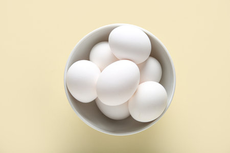 Bowl with raw chicken eggs on beige backgroundの写真素材