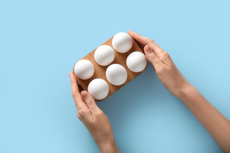 Female hands with wooden holder of raw chicken eggs on blue backgroundの写真素材