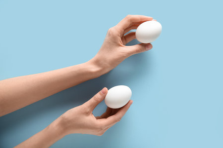 Female hands with raw chicken eggs on blue backgroundの写真素材