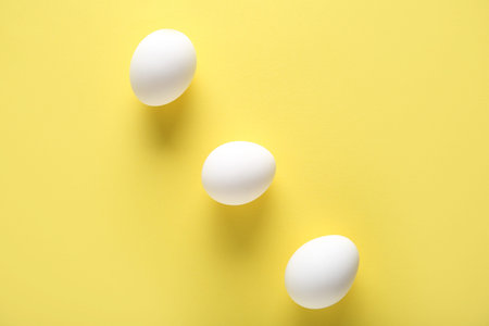 Raw chicken eggs on yellow background