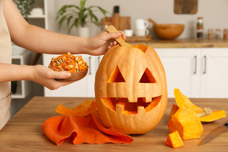 Woman with bowl of seeds, spoon and carved Halloween pumpkin on counter in kitchenの写真素材