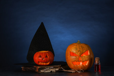 Halloween composition with jack-o-lantern, witch hat, spell book and bottle of poison on table near blue wallの写真素材