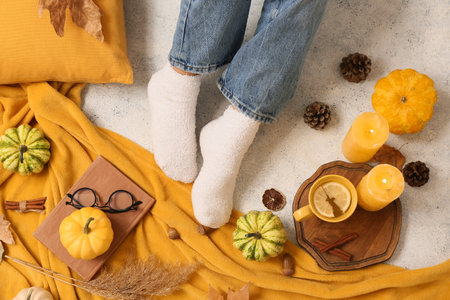 Female legs in warm socks with autumn pumpkins, plaid, candles and cup of tea on grunge white...