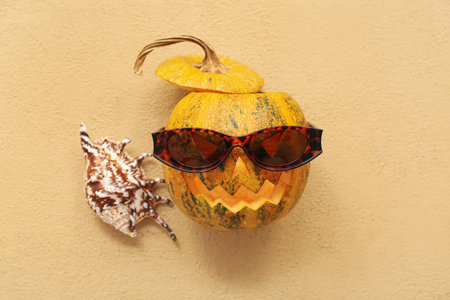 Halloween pumpkin with sunglasses and seashell on beige backgroundの写真素材