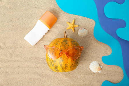 Halloween pumpkin, sunscreen cream, seashells and sunglasses on sand