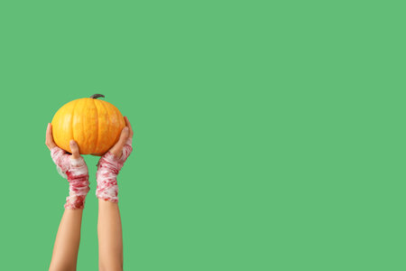 Mummy hands with ripe pumpkin on green background. Halloween celebrationの写真素材