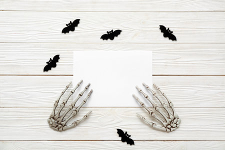Composition with blank card, skeleton hands and bats on light wooden backgroundの写真素材