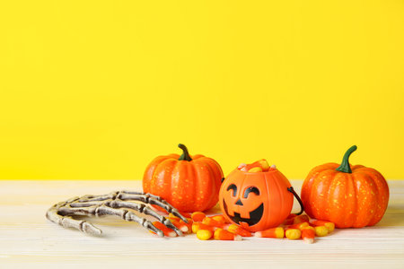 Halloween composition with toys and candies on wooden table against yellow backgroundの写真素材