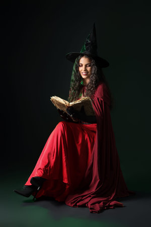 Young witch with spell book on dark background