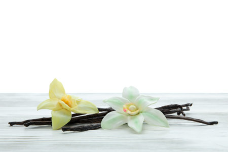 Aromatic vanilla pods and flowers on table against white background