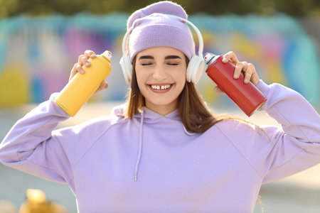 Teenage girl with spray paints listening to music outdoorsの写真素材