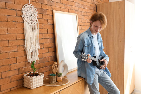 Redhead teenage boy playing ukulele at homeの写真素材