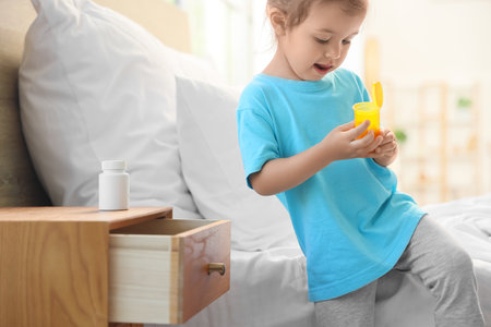 Cute little girl with pill bottle in bedroom. Child at riskの写真素材