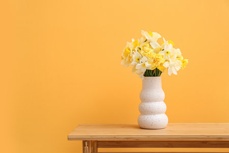 Vase with narcissus flowers on table against orange backgroundの写真素材