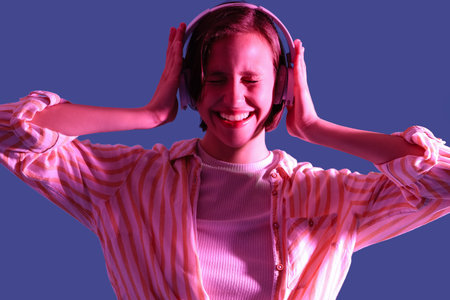Young woman in headphones listening to music on purple background, closeupの写真素材