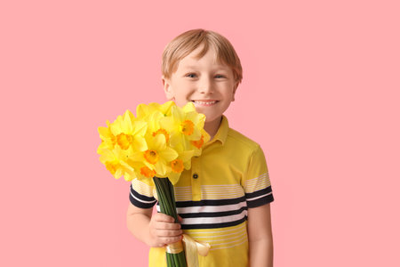 Cute little happy boy with bouquet of beautiful narcissus on pink background