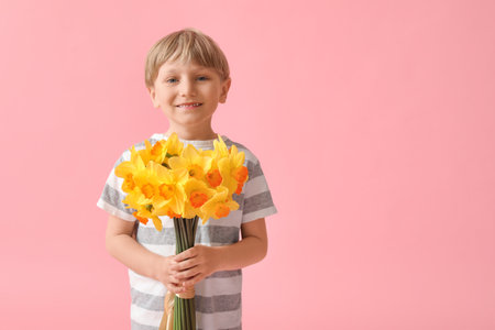 Cute little happy boy with bouquet of beautiful narcissus on pink backgroundの写真素材