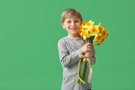 Cute little happy boy with bouquet of beautiful narcissus on green backgroundの写真素材