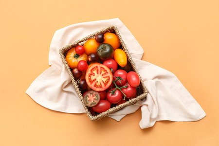 Wicker box with different fresh tomatoes on orange backgroundの写真素材