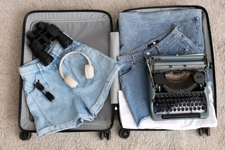 Open suitcase with vintage typewriter and clothes on carpet, top viewの写真素材