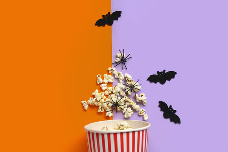 Bucket with tasty popcorn, bats and spiders for Halloween on color backgroundの写真素材