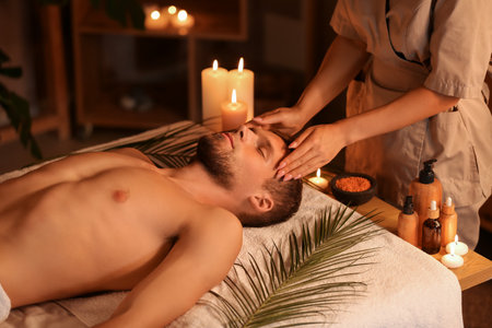 Young man getting treatment head massage on couch in dark spa salonの写真素材