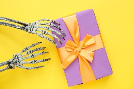 Halloween gift and hands of skeleton on yellow background. Top view
