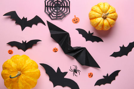 Paper bats with spider, web and fresh pumpkins for Halloween party on pink background