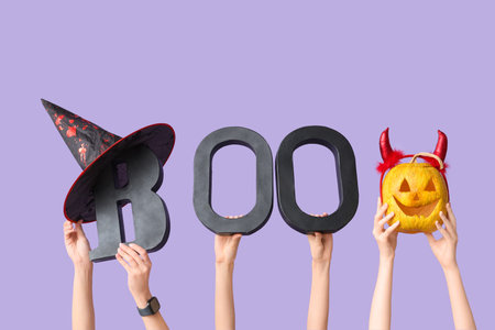 Female hands with letters BOO, witch hat and pumpkin on lilac background. Halloween celebration